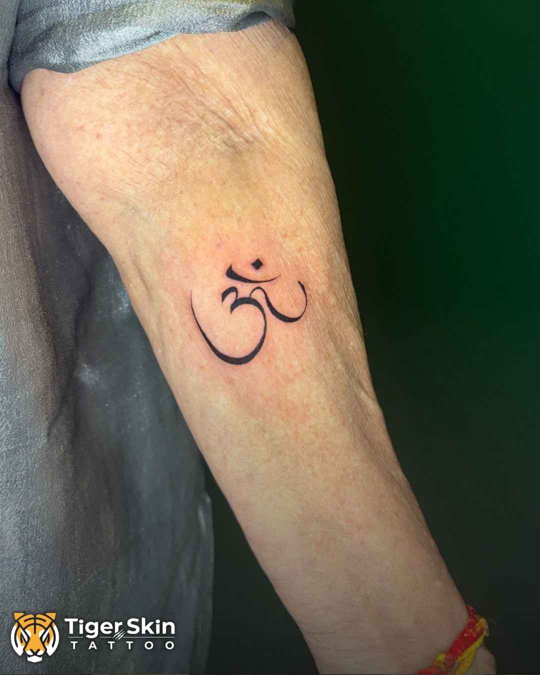 Om tattoo on Mai's wrist by Swarain Pawar, Tiger Skin Tattoos Thane